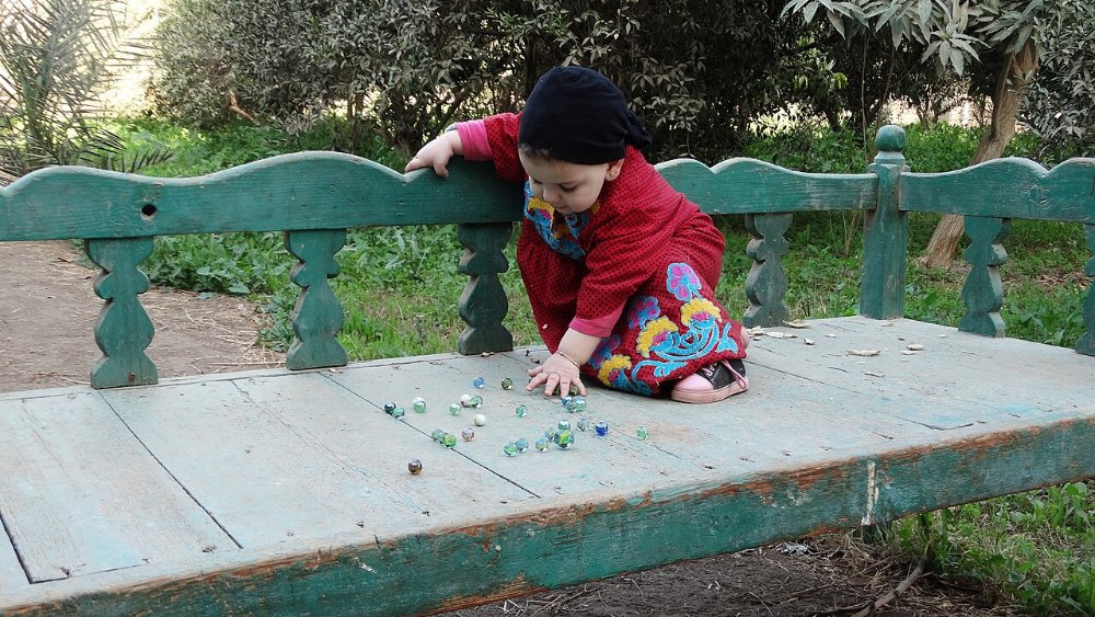 ילד משחק בגולות זכוכית צבעוניות על ספסל עץ בגן